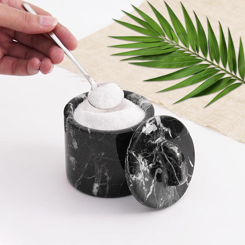 Hand holding spoon with Himalayan pink salt from a black marble salt cellar with lid – ideal salt and sugar container for kitchen use