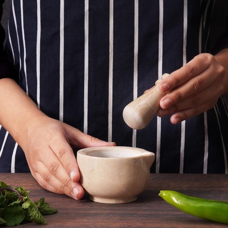 Hand using verona marble mortar and pestle to crush herbs and spices on kitchen counter