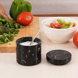 Black marble salt cellar with spoon placed between fresh vegetables on cutting board