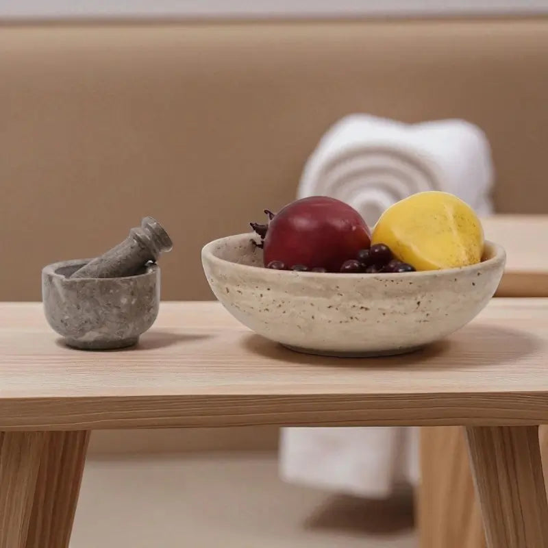 Travertine fruit bowl filled with autumn fruits and a marble mortar and pestle on a wooden table, styled for cozy fall kitchen and home décor event