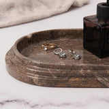 Close-up of an oceanic marble oval tray holding rings and earrings, used for storing jewelry and perfume on a bathroom countertop.