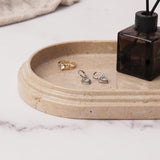 Close-up of an verona marble oval tray holding rings and earrings, used for storing jewelry and perfume on a bathroom countertop.