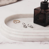 Close-up of white marble oval tray holding rings and earrings, used for storing jewelry and perfume on a bathroom countertop.