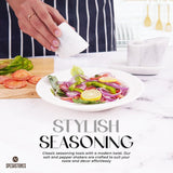 Hand sprinkling salt on fresh salad using marble salt and pepper shakers with tray in white