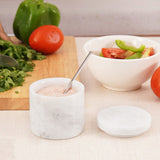 white marble salt cellar with spoon placed between fresh vegetables on cutting board